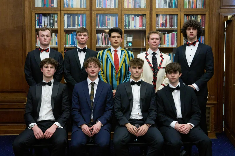 A group in black tie and blazers posing in front of library shelves