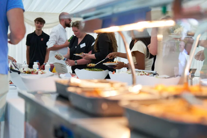Food on a buffet table with guests serving themselves in the background