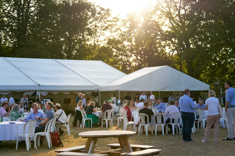 Guests seated beside a marquee under trees in golden evening sunlight