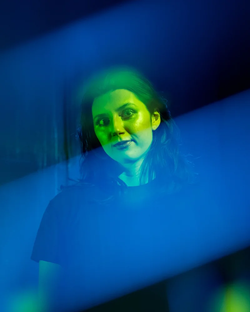 A person looking towards the camera under green light, framed by bands of blue light