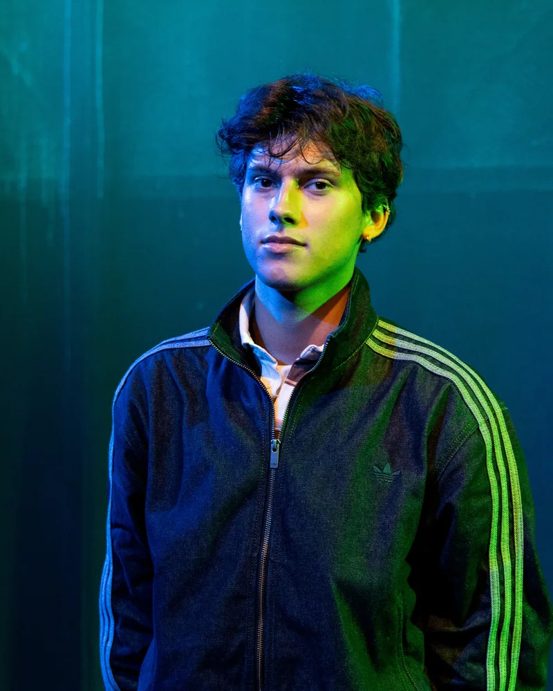 A person in a dark zip-up jacket looking towards the camera under blue and green light